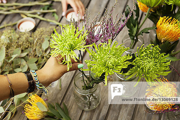 Cropped image of woman arranging flowers in jars on table