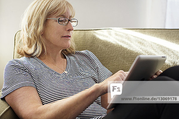 Nahaufnahme einer Frau  die einen Tablet-Computer benutzt  während sie zu Hause auf dem Sofa sitzt