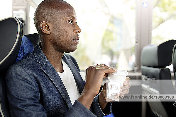 Man looking away while holding disposable cup in bus