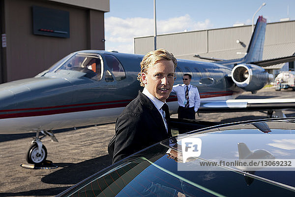 Porträt eines Geschäftsmannes  der im Auto gegen ein Flugzeug steht
