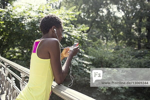 Frau benutzt Mobiltelefon  während sie sich im Park an ein Geländer lehnt