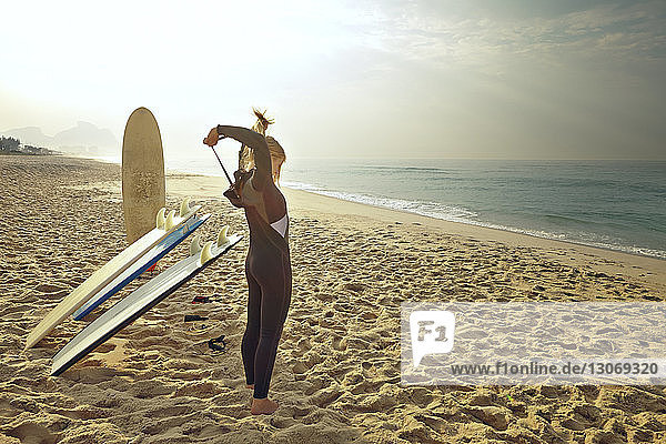 Frau  die einen Neoprenanzug mit Reißverschluss trägt  während sie am Strand an den Surfbrettern steht