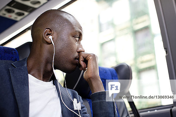 Nachdenklicher Mann mit Kopfhörer schaut weg  während er im Bus sitzt