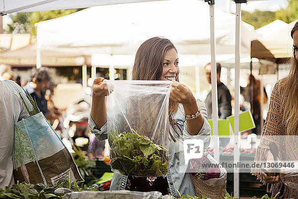 Lächelnde Frau mit Freundin beim Gemüseeinkauf am Marktstand