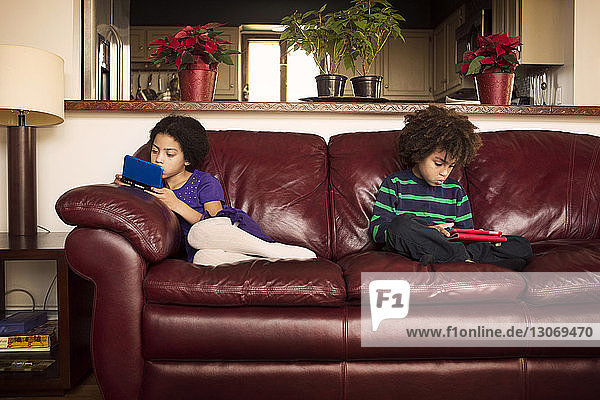 Bruder und Schwester nutzen Technologien  während sie zu Hause auf einem Ledersofa sitzen