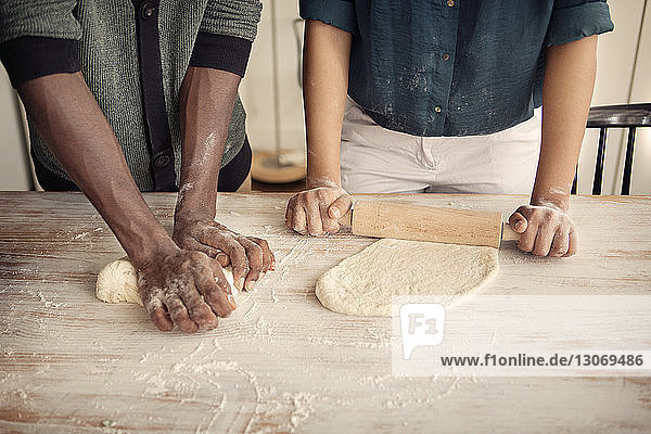 Midsection of couple kneading and rolling dough at table