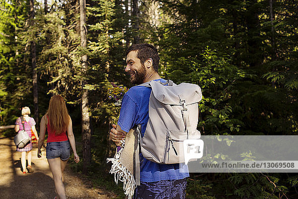 Lächelnder Mann mit Rucksack  der mit Mutter und Schwester an Bäumen im Wald spazieren geht