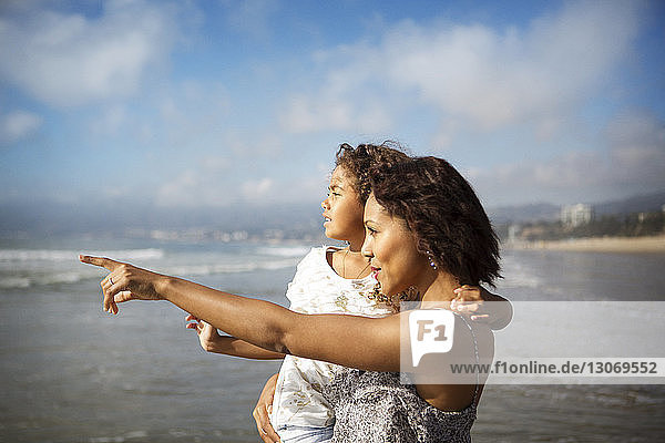 Frau  die eine Tochter trägt und auf sie zeigt  während sie am Strand am Ufer steht
