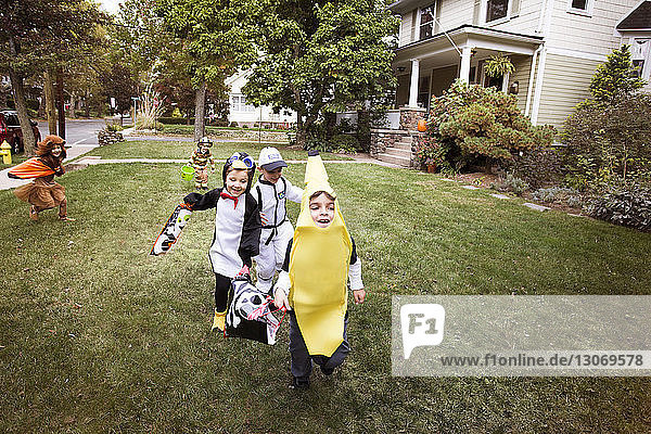 Kinder in voller Länge in Halloween-Kostümen  die während eines Streiches oder einer Behandlung im Hof laufen