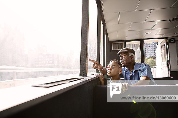 Großvater  der auf ein Fenster zeigt und einem Mädchen auf der Fähre zeigt