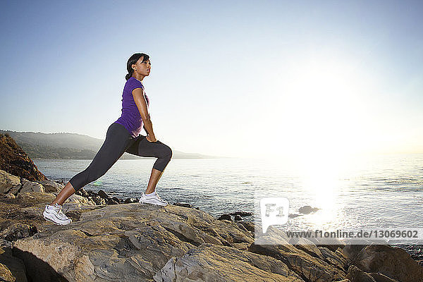 Side view of woman exercising on rocks against sea