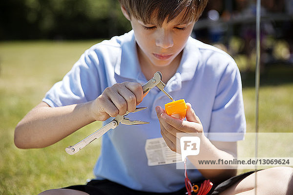 Boy working on object with tool while making craft at park