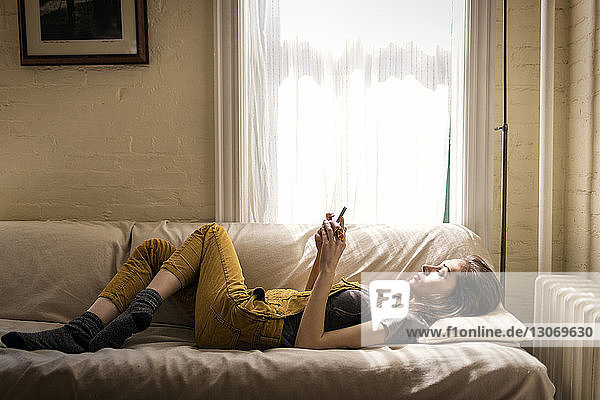 Side view of woman using smart phone while relaxing on sofa at home