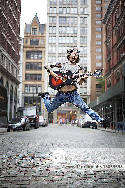 Mann springt beim Gitarrespielen auf der Straße in der Stadt