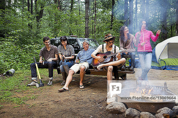Friends enjoying while sitting by picnic table in forest