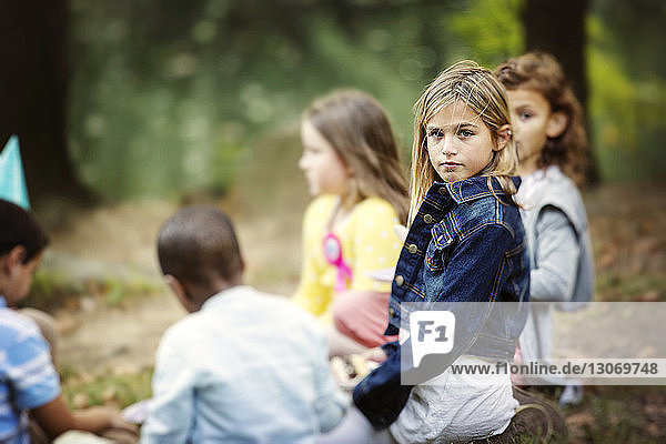 Portrait of girl sitting with friends on field at park