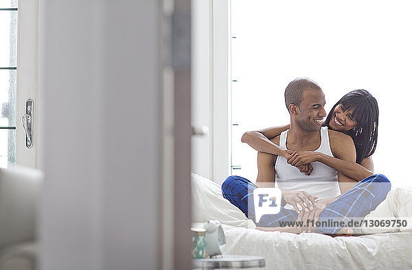 Frau umarmt Mann  während sie zu Hause auf dem Bett sitzt