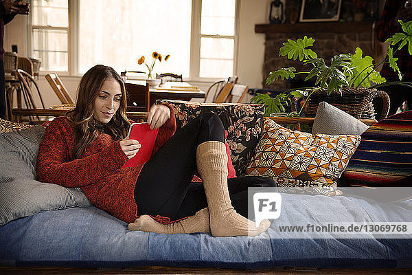 Frau liest Buch  während sie zu Hause auf dem Sofa sitzt