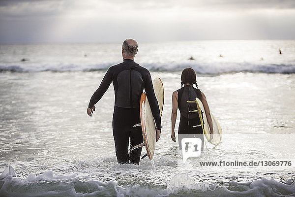 Rear view of senior couple carrying surfboards while walking in sea