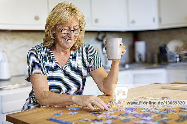 Glückliche Frau hält Becher  während sie zu Hause Puzzle spielt