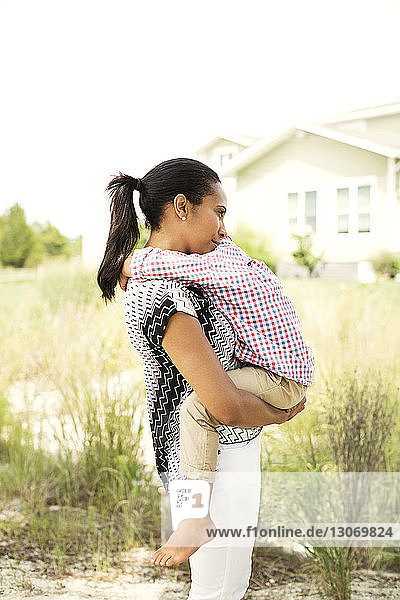 Happy woman embracing son while standing in backyard against clear sky