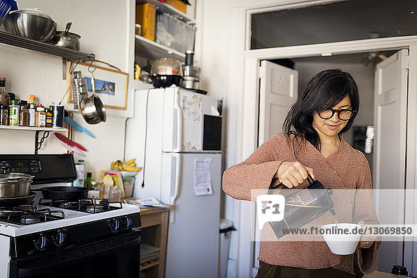 Frau gießt Kaffee in Tasse ein  während sie in der Küche steht