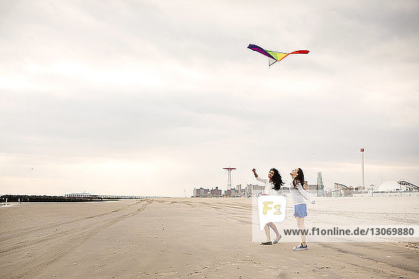 Female friends flying kite at beach