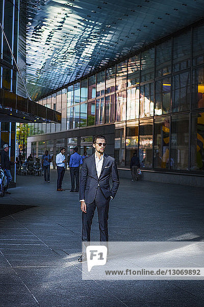 Businessman standing on street amidst modern buildings in city