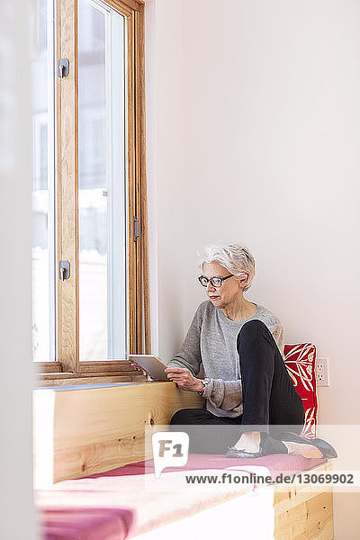 Ältere Frau benutzt Tablet-Computer  während sie zu Hause sitzt