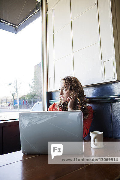Frau mit Laptop-Computer schaut weg  während sie im Café sitzt