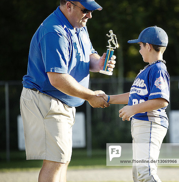 Coach giving trophy to boy on baseball field