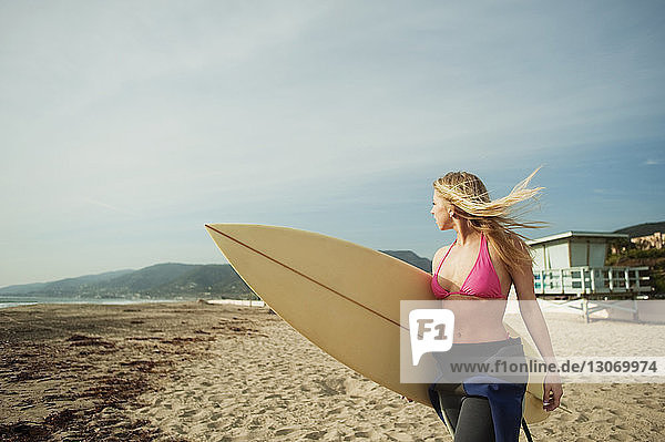 Frau mit Surfbrett  die beim Strandspaziergang am Ufer wegschaut