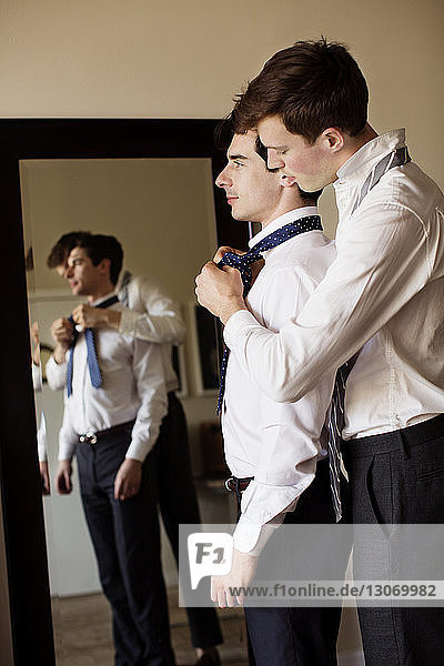 Side view of gay man assisting boyfriend for tying necktie