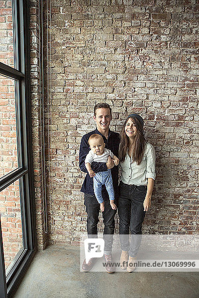 Happy family standing against brick wall at home