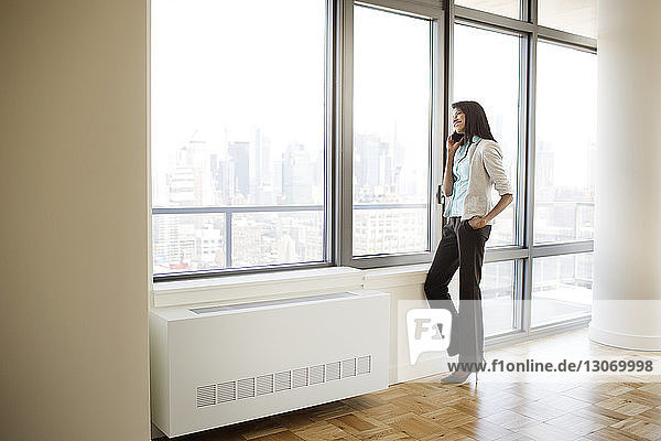 Businesswoman talking on mobile phone while standing by window in office