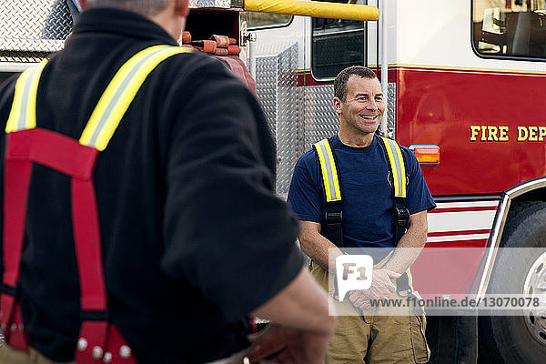 Happy fireman standing by coworker against fire engine