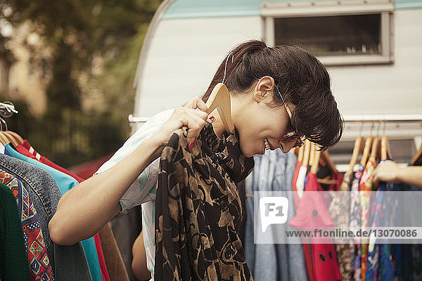 Side view of woman checking dress while standing by clothes rack