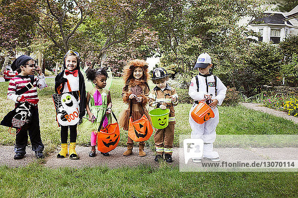 Kinder in voller Länge in Halloween-Kostümen  die während eines Streiches oder einer Behandlung auf dem Weg stehen