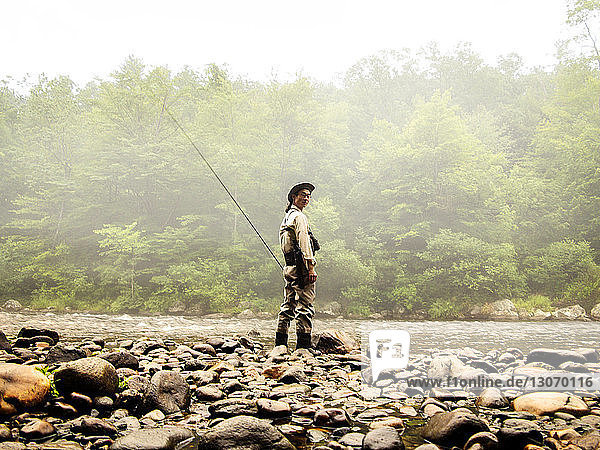 Portrait of man holding fishing rod while standing by river