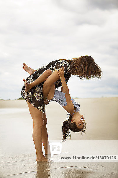 Glückliche Mutter spielt mit Tochter am Strand vor bewölktem Himmel