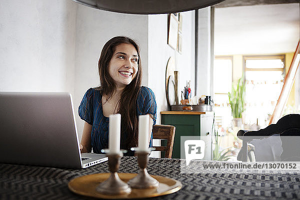 Frau schaut weg  während sie mit Laptop-Computer am Tisch sitzt