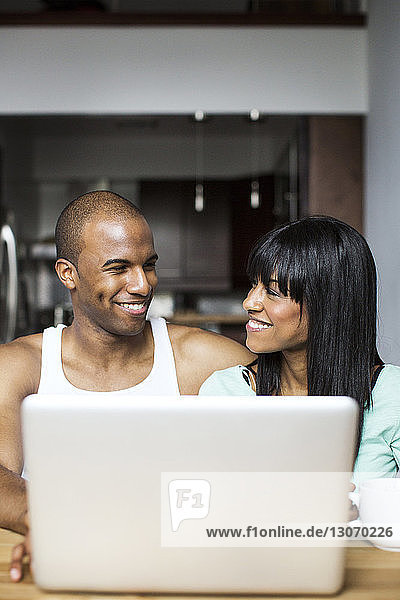 Smiling couple using laptop computer while sitting by table at home