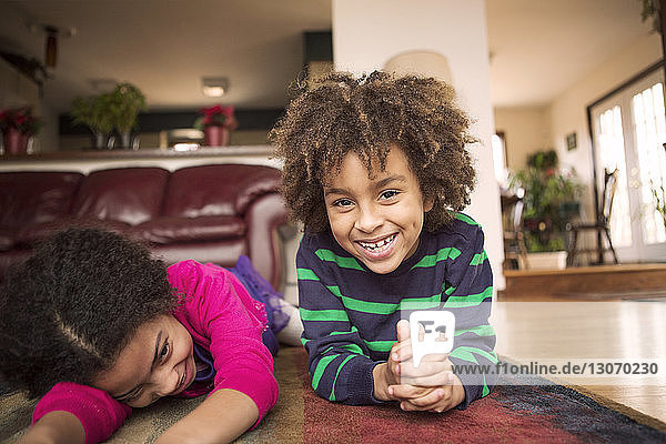 Porträt eines glücklichen Jungen  der mit seiner Schwester zu Hause auf dem Teppich liegt