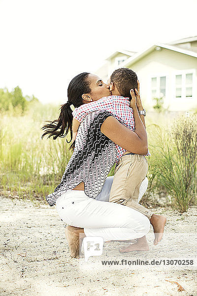 Happy woman kissing son in backyard against clear sky