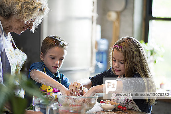 Children with grandmother preparing dough in kitchen