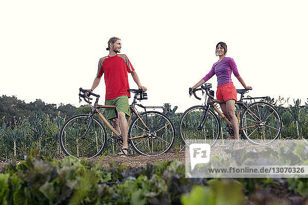 Low angle view of couple with bicycles standing at farm against clear sky