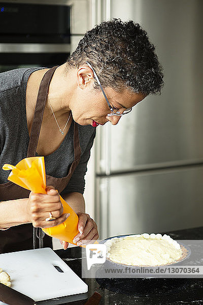 Woman piping cream on tart at home