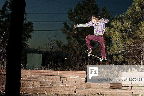 Mann springt nachts mit Skateboard