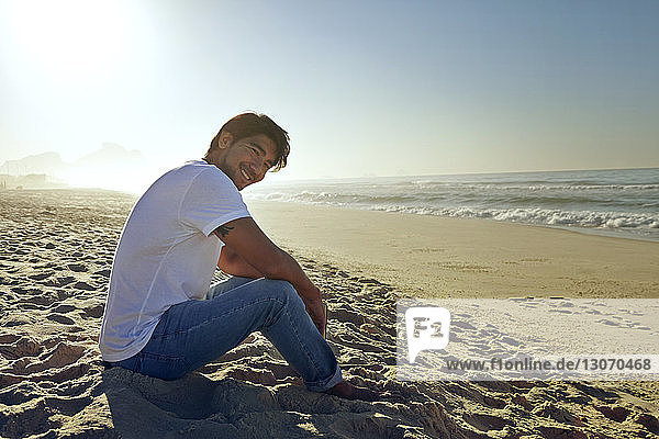 Porträt eines lächelnden Mannes  der auf Sand am Strand sitzt