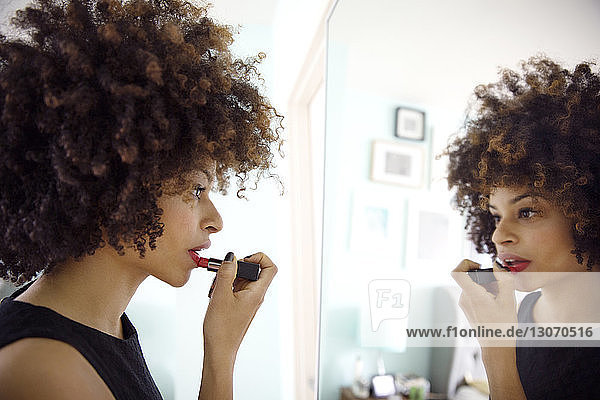 Side view of woman applying lipstick while looking at mirror